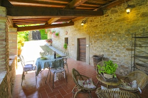 A rustic outdoor patio with stone walls, a wooden ceiling, and wicker furniture.