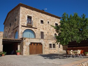 A stone building with a wooden door, a balcony, and outdoor seating.