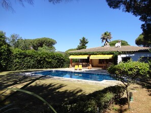 A pool area with a house in the background, surrounded by greenery.