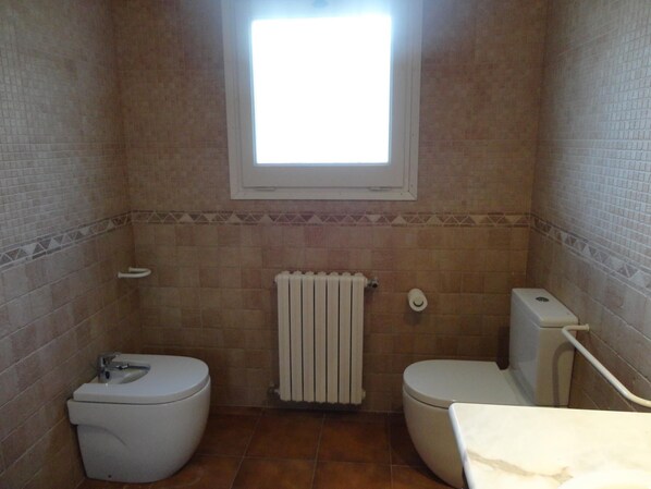 A small bathroom with two toilets, a window, and a radiator.