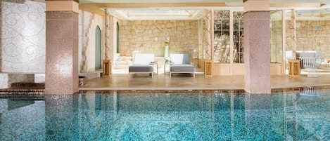 A luxurious indoor pool area with a stone wall and two lounge chairs.