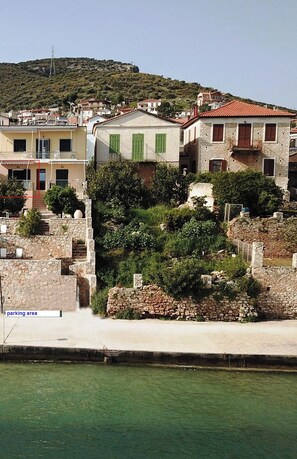 A coastal town with stone buildings, a clear view of the sea, and a parking area.