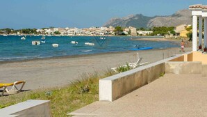 A coastal view with a beach, boats, and buildings in the background. - Sa Marina 7A, villa direct on the beach (Alcudia - Puerto de Alcudia)