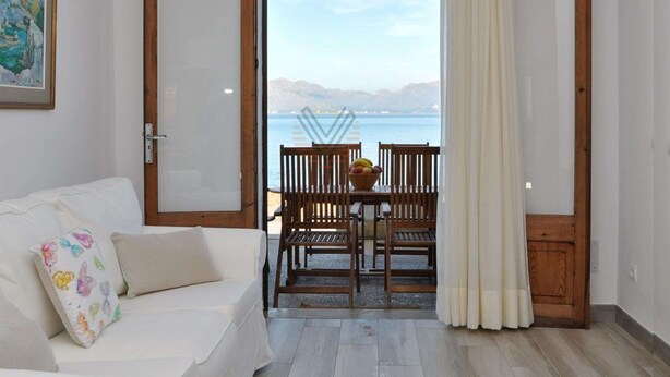A room with a white sofa, a wooden table with chairs, and a view of the sea through an open door. - Sa Marina 7A, villa direct on the beach (Alcudia - Puerto de Alcudia)