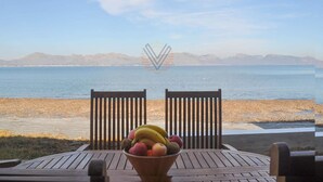 A wooden table with a bowl of fruit and two chairs facing a beach with mountains in the background. - Sa Marina 7A, villa direct on the beach (Alcudia - Puerto de Alcudia)