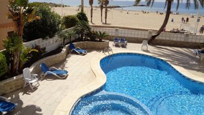Una piscina con sillones de descanso, vista a la playa y palmeras.