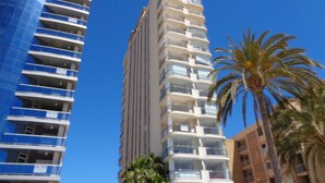 Un edificio alto con varios balcones, rodeado de palmeras y otros edificios.