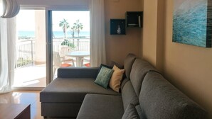 Una sala de estar con un sofá gris, una mesita y vista al mar a través de un ventanal corredero.
