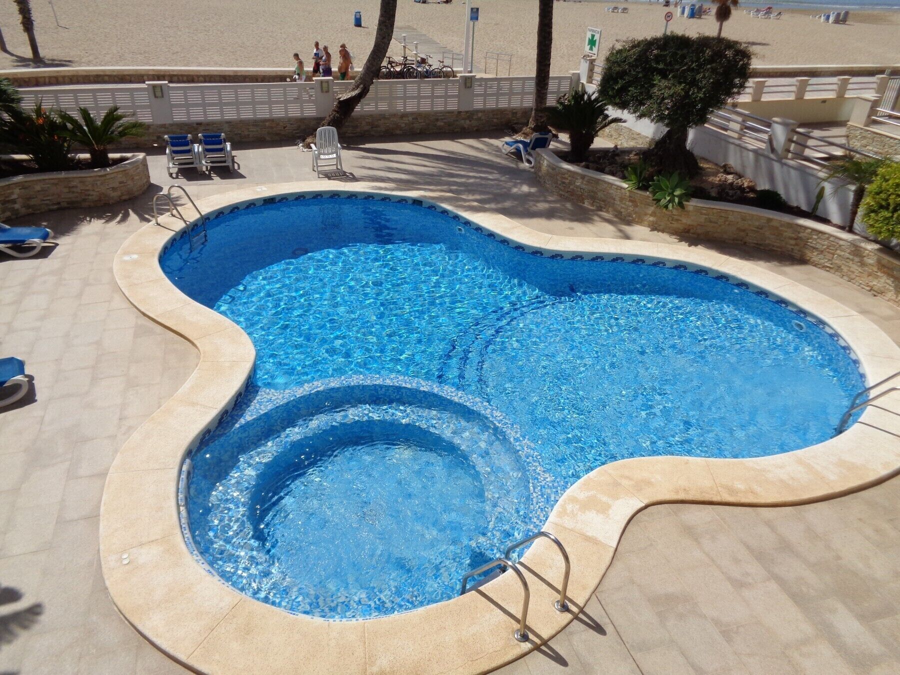 Une piscine au design incurvé, entourée de chaises longues et offrant une vue sur la plage.