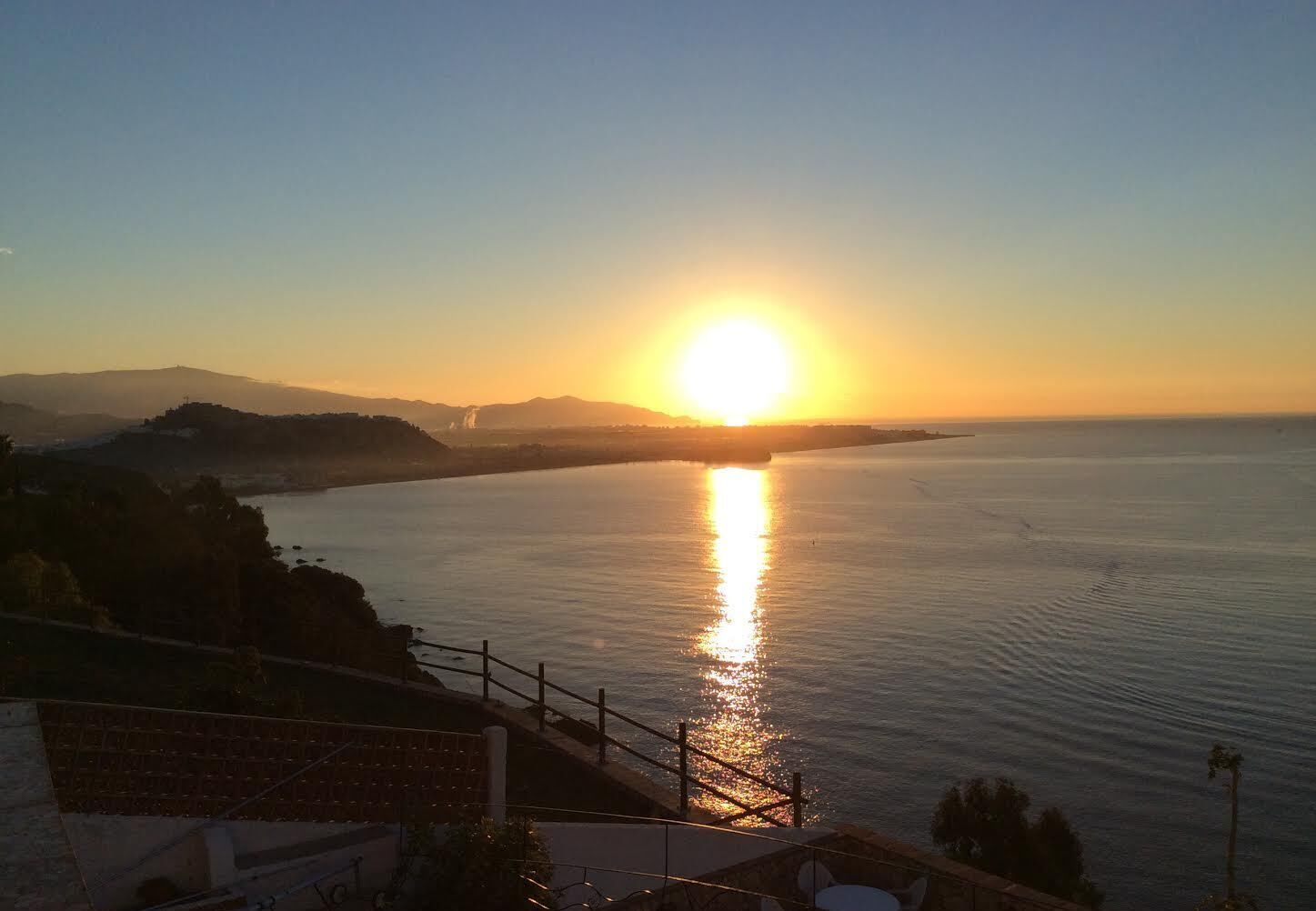 Un coucher de soleil sur une étendue d'eau calme, avec une chaîne de montagnes en arrière-plan.