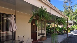 Un espacio de estar al aire libre cubierto, con una mesa y sillas, rodeado de plantas en macetas y una valla de madera.