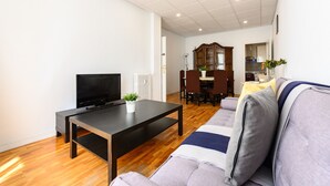 Una sala de estar con televisión de pantalla plana, una mesa de centro, un sofá y un comedor con un aparador y sillas.