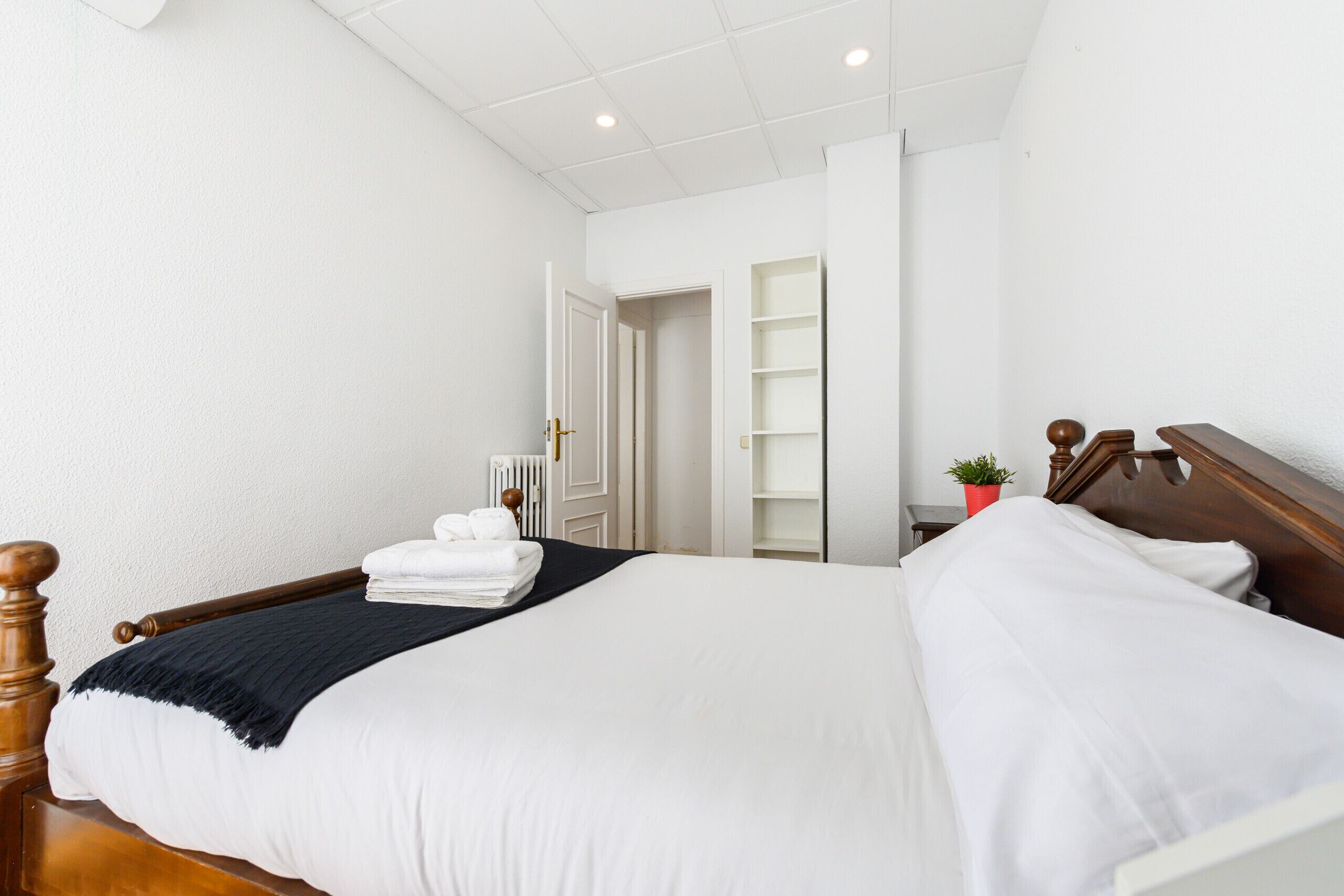 Un lit bien fait, avec du linge de lit blanc et une couverture sombre, une tête de lit en bois et un radiateur en arrière-plan.
