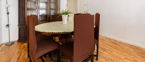 Un comedor con una mesa redonda, sillas tapizadas en tonos marrones, un mantel blanco y un aparador de madera con puertas de cristal.