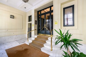 Un escalier en marbre, avec des rampes en laiton, mène à une porte en bois sombre.