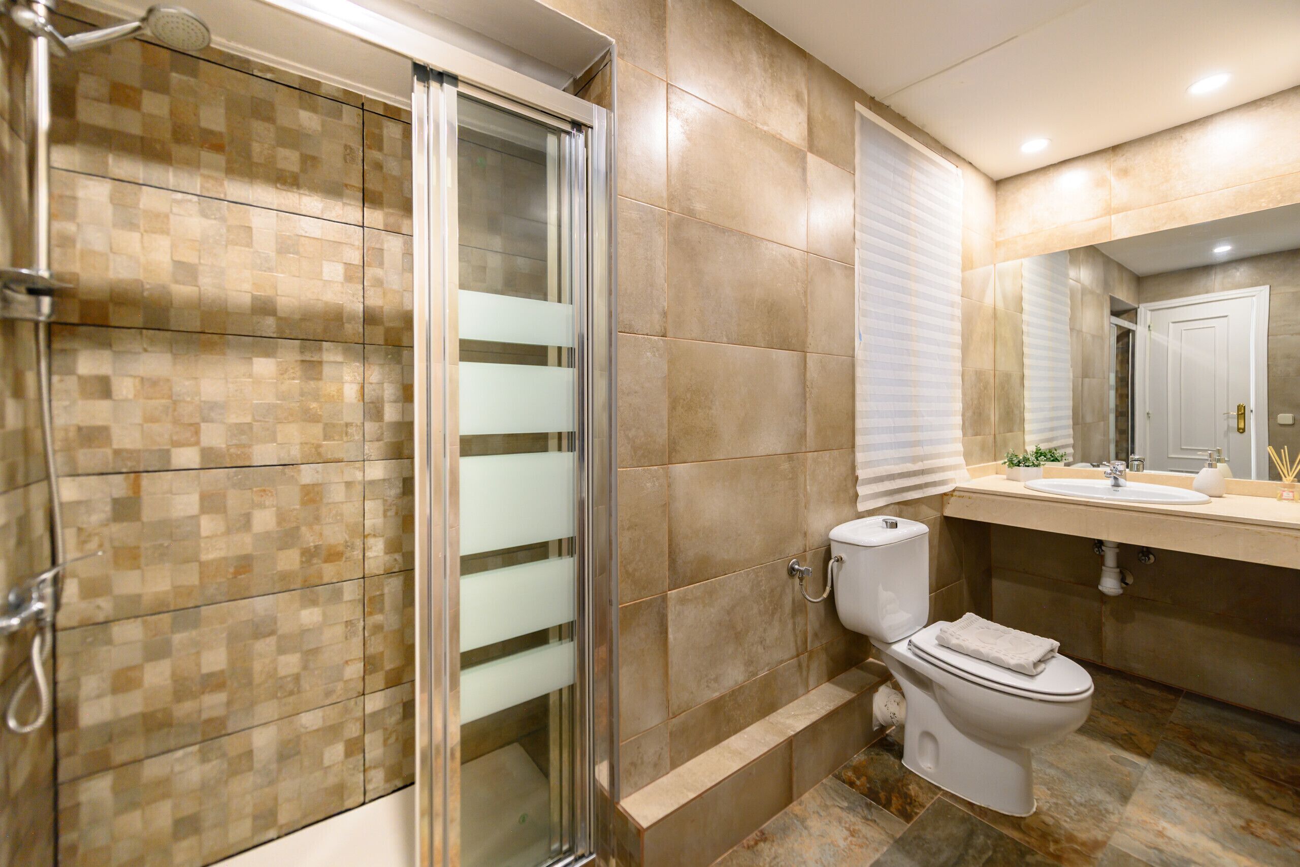 Un baño con cabina de ducha de vidrio, inodoro y lavamanos con espejo.