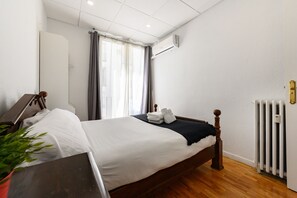 Une chambre d’hôtel avec un lit en bois, du linge de lit blanc, un radiateur et une plante en pot.