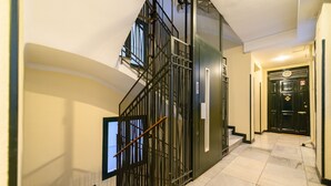 Una escalera con barandilla metálica, una puerta con cerradura de seguridad y suelo de baldosas.