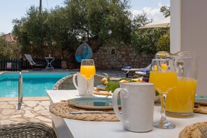 Desayuno junto a la piscina con una mesa, platos, vasos y una jarra de jugo de naranja.