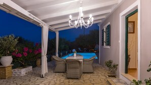 Une terrasse extérieure avec un sol en pierre, des meubles en osier et une piscine en arrière-plan.