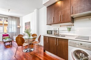 Une cuisine compacte dotée de meubles en bois, d’un four à micro-ondes, d’un lave-linge et d’un coin repas avec une table et des chaises en verre.