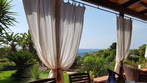 A table set for dining with a view of the sea, curtains, and lush greenery. - Lisca Blu villa 6+2 pp, seaside, A/C, Wifi, free parking and 2 bathrooms. Dogs allowed (Custonaci)