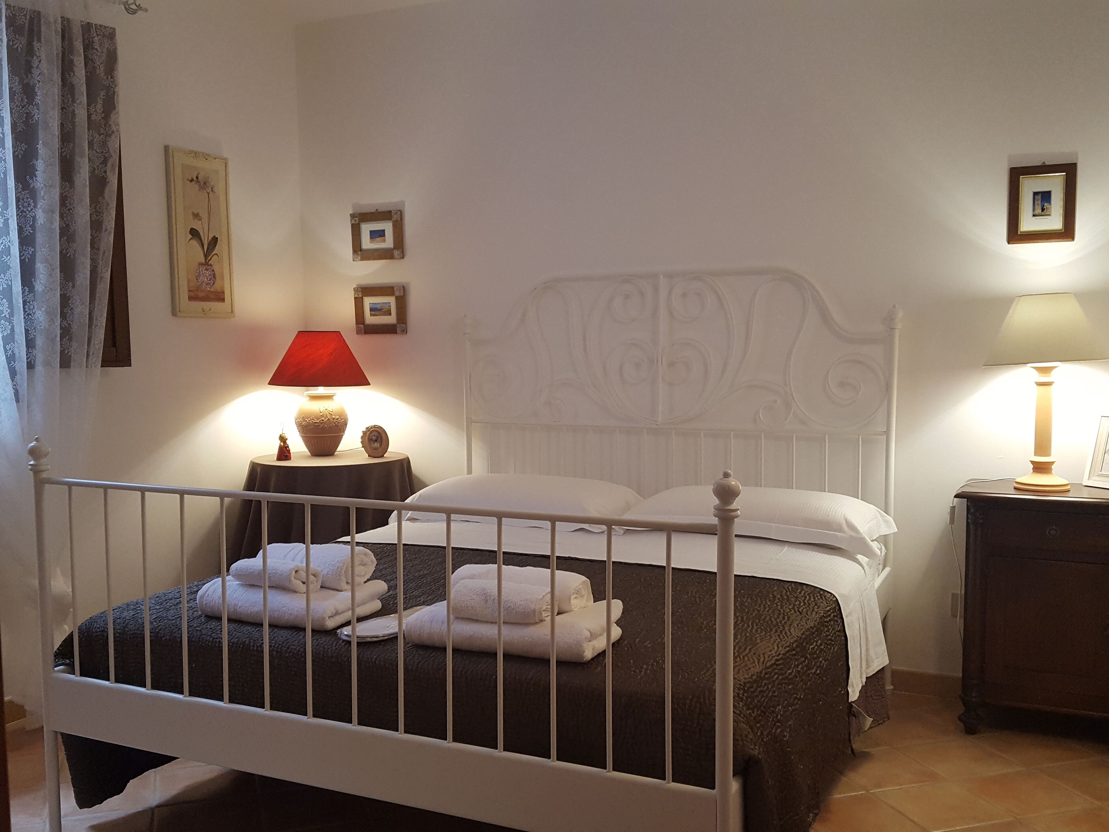 A neatly made bed with white linens and a headboard, a bedside table with a lamp, and a small picture frame on the wall.