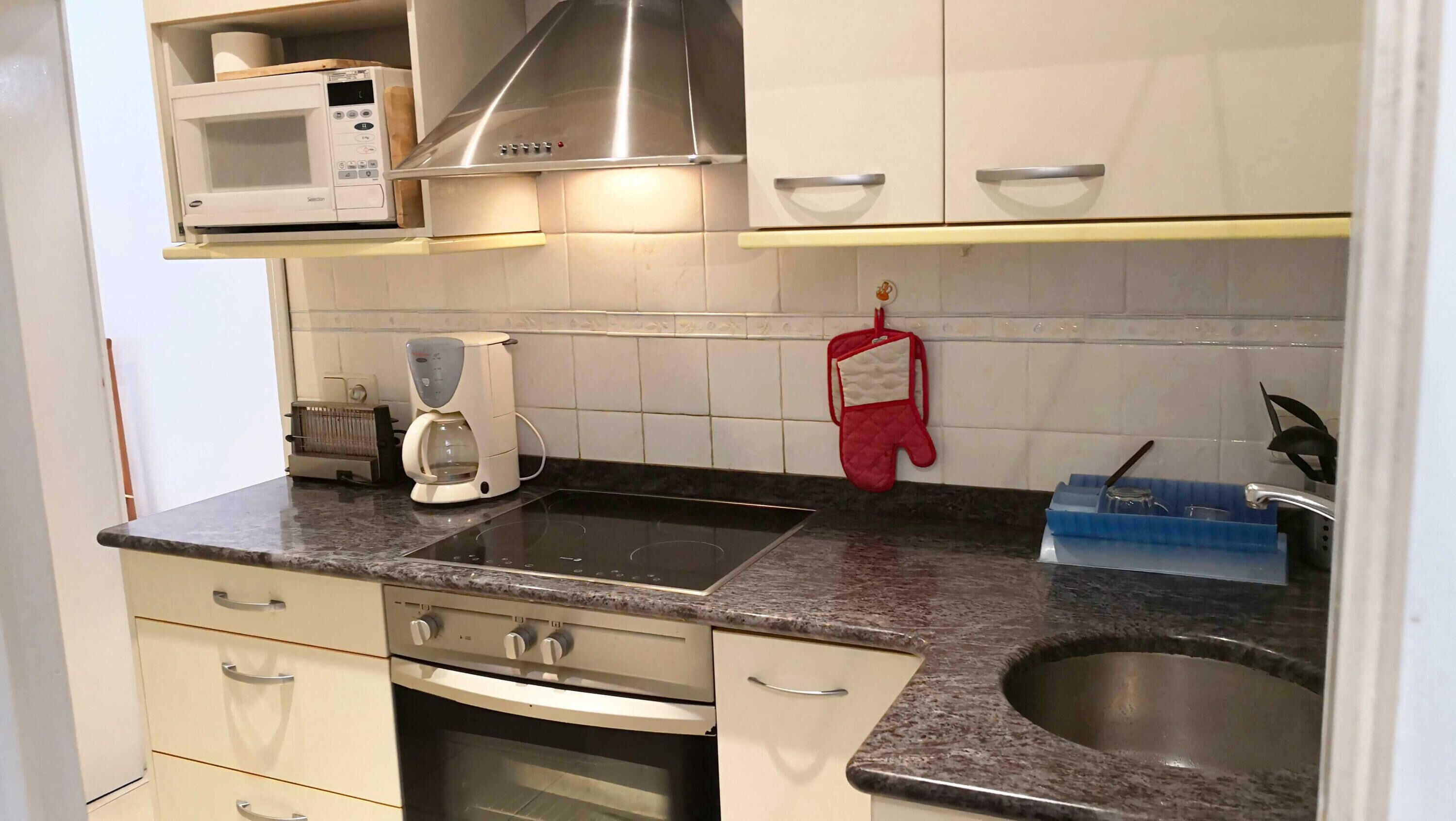 Een keuken met een magnetron, koffiezetapparaat, oven en een roestvrijstalen spoelbak.
