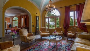 A spacious room with a large chandelier, multiple armchairs, a round coffee table, and a large window with curtains. - Casa Matteucci     . (Capannori)