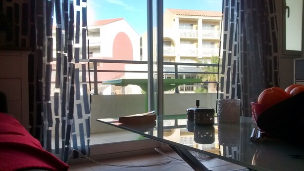 A room with a glass table, a red chair, and a view of a building with balconies. - T1 standing entrance of CALVI  (Calvi)
