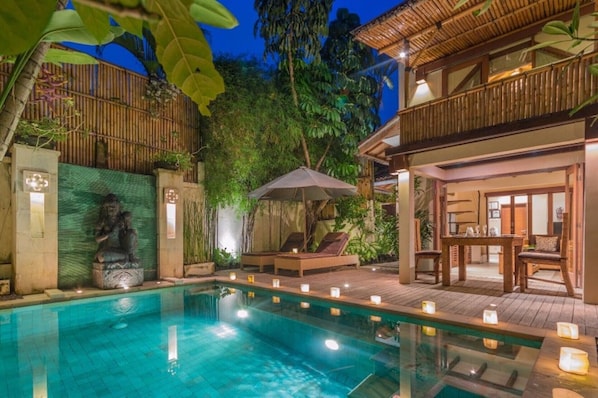 Relax by the serene pool surrounded by lush greenery and a tranquil bamboo fence.