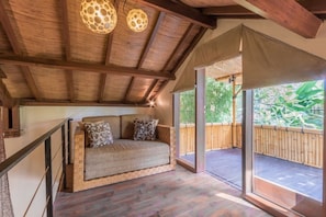 Relax in a spacious room with a sofa, wooden floor, and balcony overlooking lush greenery.