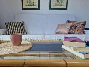 Un salon chaleureux avec un canapé blanc, un set de table en fibres naturelles, une table basse en verre et une pile de livres.