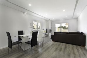 Relax in this stylish living space with a glass dining table, comfortable sofa, and large window offering a view of the outside.
