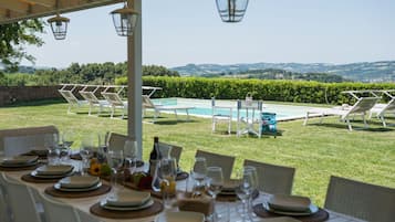 Ein Essbereich im Freien mit gedeckten Tischen, mit Blick auf einen Swimmingpool und eine schöne Landschaft.