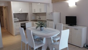 Een moderne keuken met witte kasten, een eettafel met stoelen, een kamerplant en een televisie op een kast.