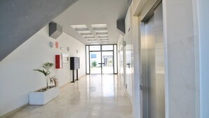 Un couloir moderne avec une porte en verre donnant sur un espace extérieur, un pot de fleurs blanc contenant des plantes et un extincteur fixé au mur.