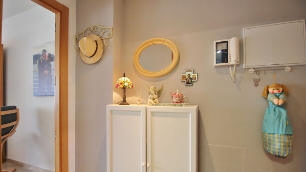 Une pièce avec une armoire blanche, un miroir, un téléphone et une poupée accrochée au mur.
