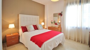 Une chambre à coucher avec un lit, des tables de chevet, une commode, un miroir et une fenêtre avec des rideaux.