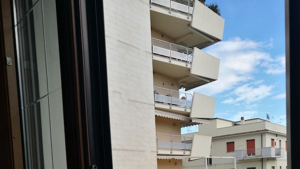 A view from a balcony with a metal railing, overlooking a street with buildings in the background. - Casa D Annunzio weekly discount + wi-fi (Pescara)