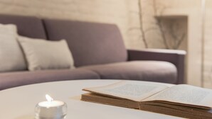 Ein Buch auf einem Tisch, eine Kerze brennt daneben, im Hintergrund ein Sofa und rechts eine Lampe.