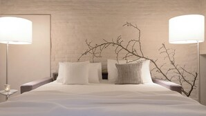 Ein ordentlich gemachtes Bett mit weißer Bettwäsche, zwei Nachttischlampen und einer Wanddekoration aus einem Zweig.