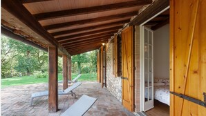 A covered outdoor area with wooden beams and a brick floor, leading to a room with a bed and a window. - La Dimora di Teresa: fairytale house in the woods, ideal for families with children. (Sovicille)