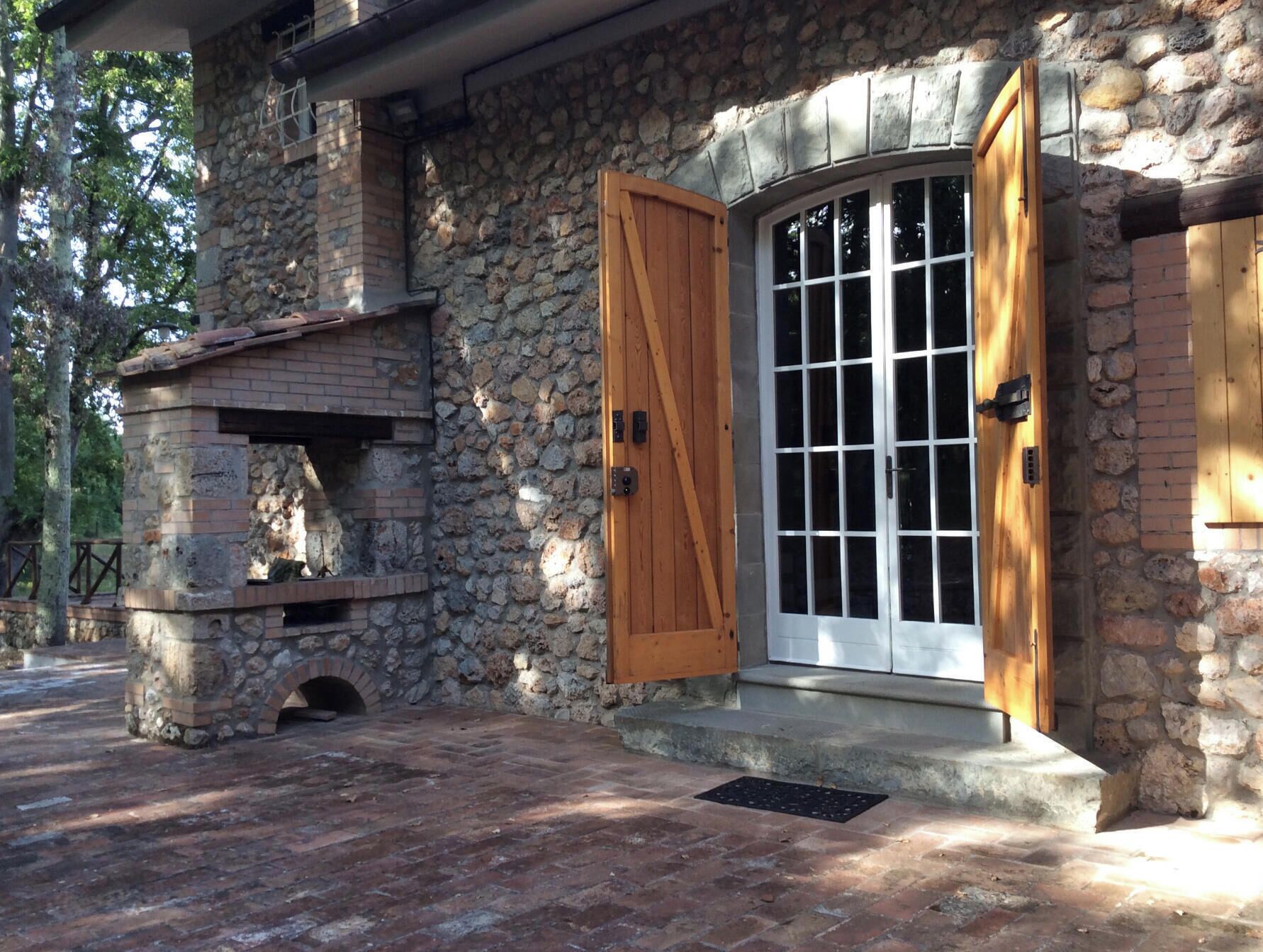 A stone building with a brick fireplace, wooden doors, and a window.