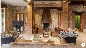 A cozy living room with a stone fireplace, comfortable seating, and a television. - La Dimora di Teresa: fairytale house in the woods, ideal for families with children. (Sovicille)