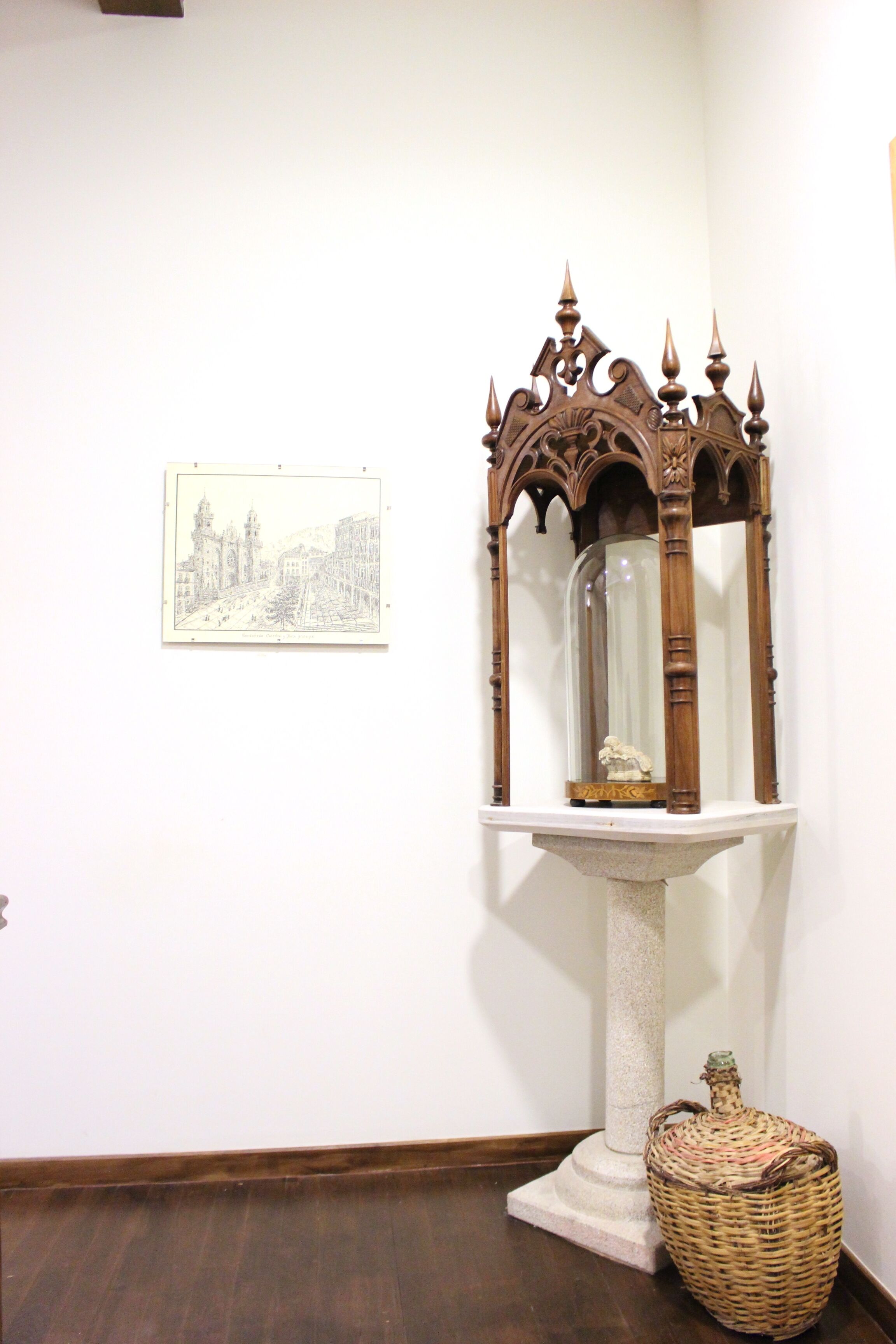 Una habitación con un pedestal de madera, un cuadro en la pared y una cesta de mimbre en el suelo.