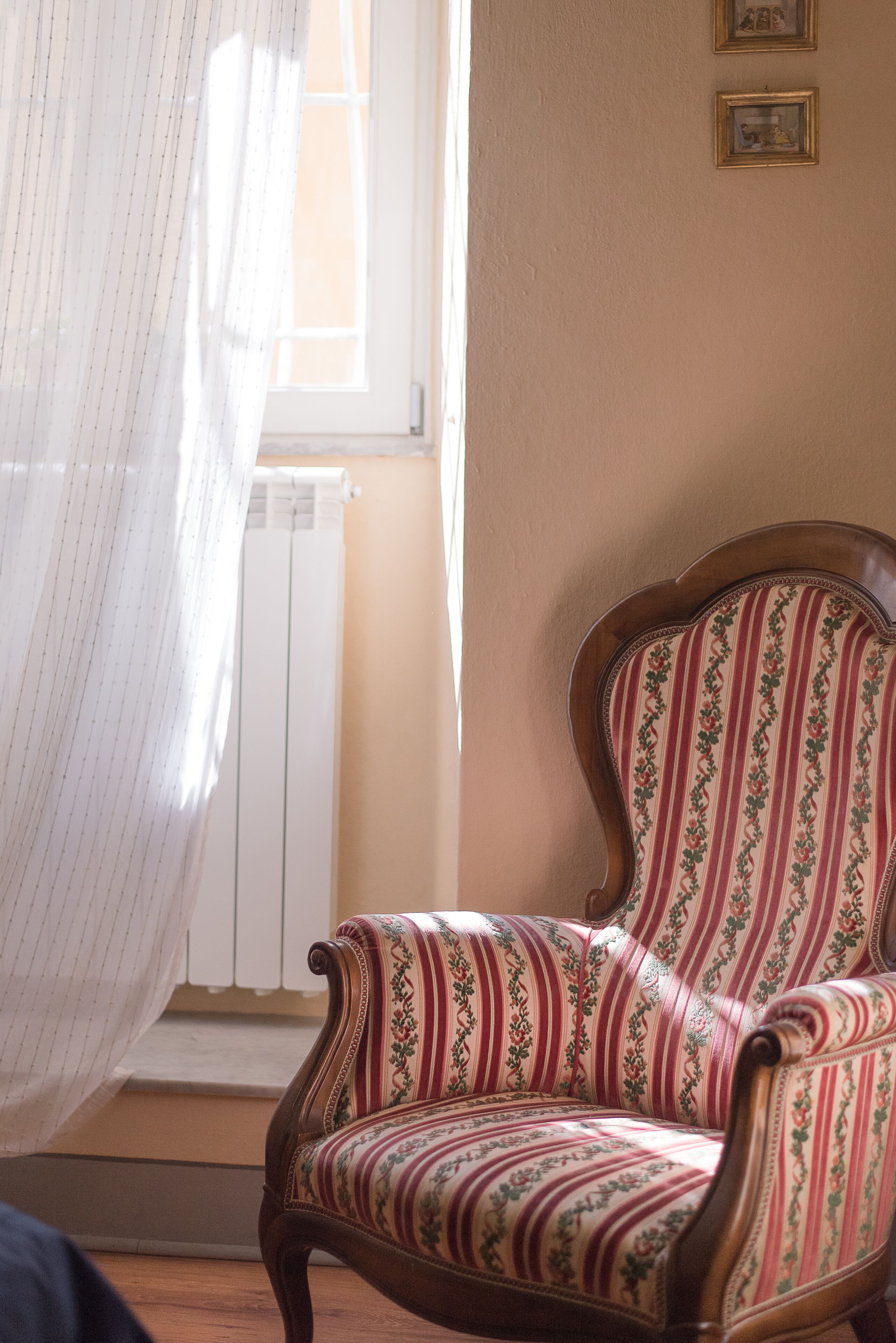 Une pièce comprenant une chaise en bois recouverte d’un tissu à rayures, un radiateur et une fenêtre avec des rideaux.