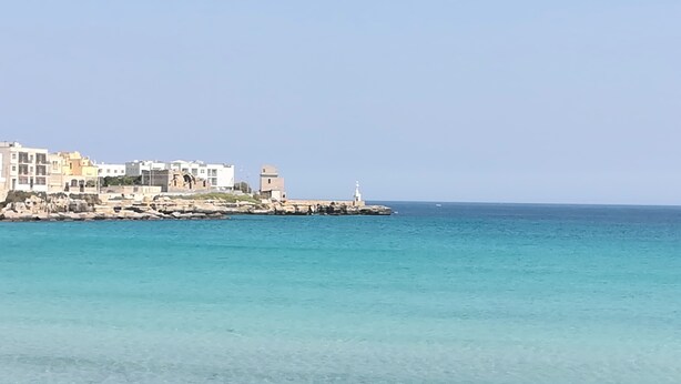 Un pueblo costero con edificios a lo largo de la orilla, un faro y un mar tranquilo.