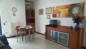 Un comedor con una mesa, sillas, un radiador, un reloj y un mueble con un televisor.