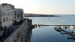 Un pueblo costero con un muro de piedra, un puerto deportivo con barcos y edificios a lo largo del paseo marítimo.